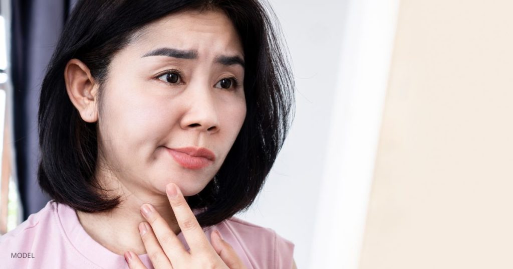 Woman experiencing facial palsy (MODEL) pointing to her chin.